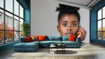 A young woman with dark hair and brown eyes is sitting with her hands on her knees. She has a serious expression on her face. a picture of an african-american woman,showing her full face Wall mural