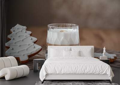 glass with cappuccino with a thick foam of milk and gingerbread in the form of a christmas tree and snowflakes with white glaze stand on a brown table on a brown background against a wooden tree Wall mural