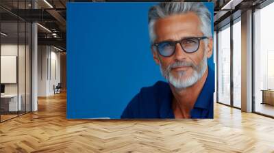 Man with a beard and glasses is smiling. He is wearing a blue shirt. The background is blue. technical writer working at the laptop, sold blue background, Wall mural