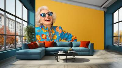 Very bright and happy old woman laughing in stylish glasses on a colored background. Close up shot of positive wrinkled old woman smiles toothily at camera wears glasses stylish outfit applies express Wall mural