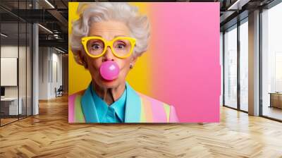 Woman in yellow jacket blowing a bubble. The bubble is pink and the woman is wearing yellow glasses. elderly woman blowing a pink bubble gum, wearing yellow glasses, jacket, vibrant color background, Wall mural