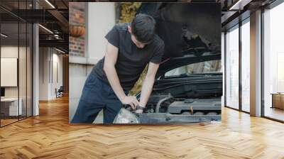 A young man takes out a headlight bulb from the open hood of a car. Wall mural