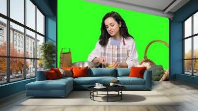 Smiling young woman slicing yellow pepper on a cutting board on the chroma key Wall mural