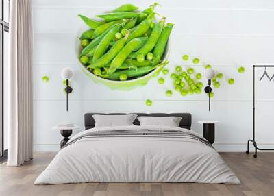 sweet green pea pods in a bowl on a white background close-up. pods of green peas and peas on the table close-up. Wall mural