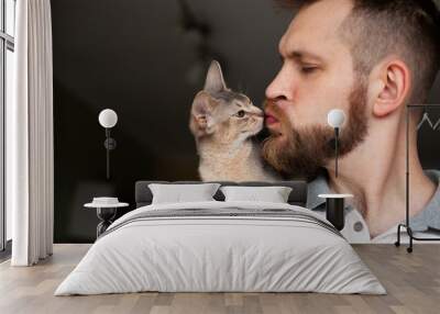 close up of bearded man kissing his grey cat sitting on his shoulder. cute abyssinian kitten of blue Wall mural