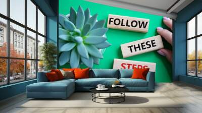 Follow these steps symbol. Wooden blocks with words Follow these steps. Beautiful green background with succulent plant. Businessman hand. Business and Follow these steps concept. Copy space. Wall mural