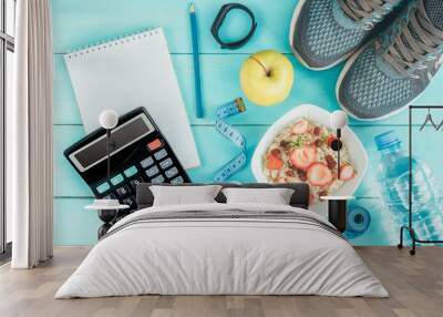 Sneakers, tape measure, notebook, calculator, bottle of water, apple and oatmeal with strawberry and raisins on blue wooden background. Healthy lifestyle, diet concept. Counting calories, menu. Wall mural