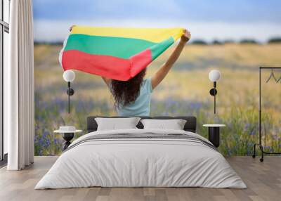 Young woman holding flag of Lithuania in a rye field with blue cornflowers. Back view. Lithuanian Flag Day. Independence restoration Day. Travel, learn lithuanian language and love Lithuania concept. Wall mural