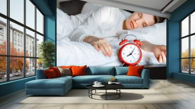 young woman sleeping comfortably on white cozy pillow. lazy single woman overslept work. Time to wake up 8 a.m early morning. Selective focus on red alarm clock. Healthy sleep lifestyle. Wall mural