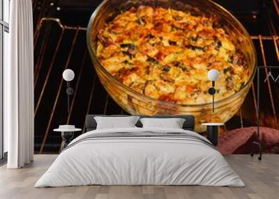 A woman takes a zucchini, mushroom and cheese casserole out of the oven in a glass dish. Zucchini recipes. Wall mural