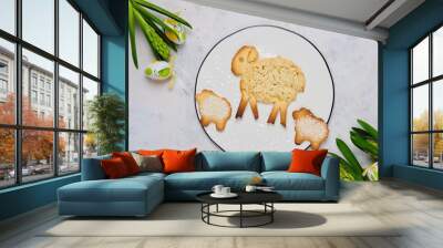 Easter pastries, a large lamb made of shortcrust pastry and two small lamb cookies on a white round ceramic board on a light concrete background with Easter decor. Wall mural