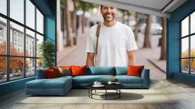 Design mockup. Waist up of young happy smiling man standing on blurred background wearing white casual t shirt looking straight at camera. Casual Casual attire  Wall mural