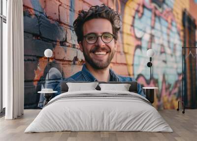 Portrait of Smiling Young Man with Beard Wearing Eyeglasses and Leaning Against Brick Wall Painted with Graffiti Wall mural