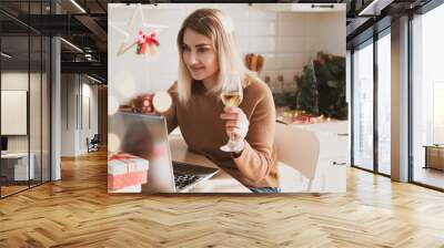 Attractive woman video chatting for christmas holidays in kitchen with glass of champagne and gifts Wall mural