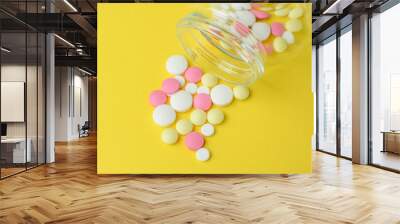 Colored pills scattered from a glass jar, against a bright yellow background. The concept of medicine and treatment for coronavirus. Side and top view. Copy space. Selective focus. Wall mural