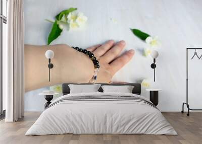 Female hand in bracelet made of natural gem stones on white background with jasmine  flowers Wall mural