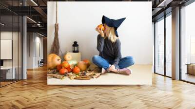 Halloween concept. Beautiful blonde girl in a witch hat with pumpkins and a broom on a white background Wall mural