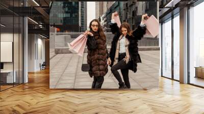 Shopping, consumption. Office center, glass buildings. Two beautiful girls are walking on the street with paper bags from shops. Shopping in the quarter of skyscrapers. Entertainment of modern women. Wall mural