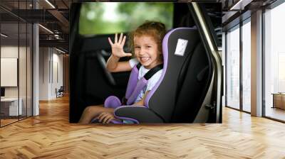 A liitle happy girl goes on a trip by car on a child safety seat summer vacation Wall mural