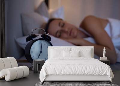 Closeup Alarm clock with blurred woman lazy in bed in background Wall mural