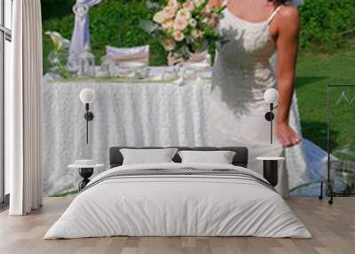 A bride with a veil and a bouquet in a white wedding dress in front of a wedding table in the garden. Wall mural