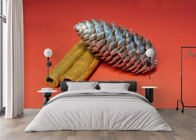 a pinecone colored silver lies next to two sticks of brown cinnamon on a red background side view . Christmas symbols Wall mural