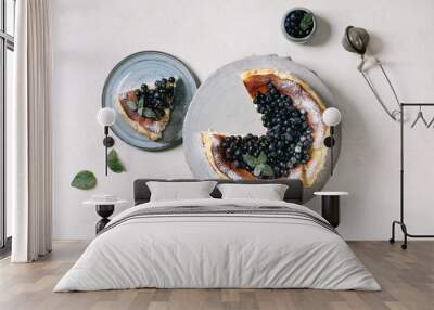 Homemade blueberry baked soft cheesecake san sebastian, whole and sliced, on ceramic plate decorated by fresh wild berries, icing sugar and mint over white texture background. Flat lay, space Wall mural