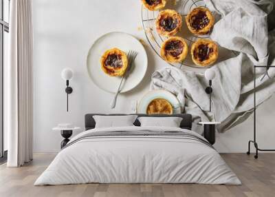 Traditional Portuguese egg tart dessert Pasteis Pastel de nata on cooling rack and ceramic plate with fork, cup of black coffee and jug of cream over white marble background. Flat lay, space Wall mural