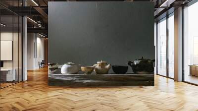 Variety of craft handmade ceramic teapots and cups for tea ceremony standing on old wooden shelf in dark room. Wall mural