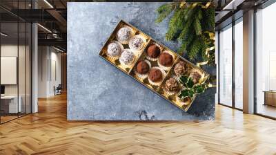 Variety of homemade dark chocolate truffles with cocoa powder, coconut, walnuts as Christmas gift in golden box with fir tree, Christmas decorations above over blue background. Top view, copy space. Wall mural