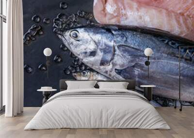 Variety of raw fresh fish. Whole tuna and herring, fillet of salmon, cod, red fish on crushed ice over dark wet metal background. Top view with space. Fish market concept Wall mural