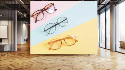 multiple eyeglasses on a multicolored background of pastel colors, geometric background, pink yellow and light blue colors, trendy eyeglass frames Wall mural