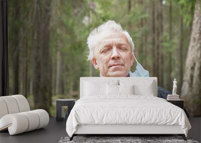 senior man takes off his surgical face mask in forest. A relaxed pensioner breathe fresh air Wall mural