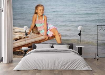 Cute little girl on the beach. Baby is resting near the sea. Summer holidays. Girl in summer. Beautiful little girl lies on pier near water. girl lying on a wooden bench on the beach.  Wall mural