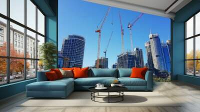 Tower cranes working against a clear blue sky, with cityscape and tall buildings in the background, showing urban development Wall mural