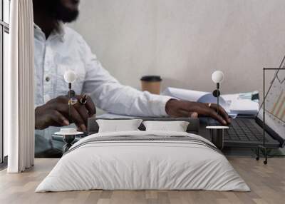 African American man working with laptop computer and using calculator, making financial audit, reviewing bills tax and accounting in living room. Black guy do freelance work at home office Wall mural