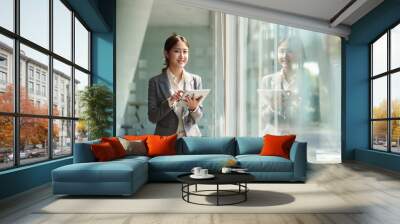 attractive business asian woman standing near window and using smart digital tablet. Wall mural