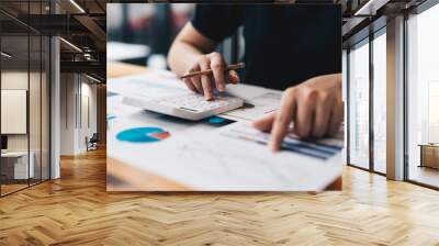 Close up of business woman or accountant hand holding pen working on calculator to calculate business data, accountancy document and laptop computer at office, business concept Wall mural