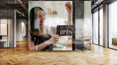 Portrait of smiling young barista girl in apron holding open sign board while standing at her cafe. elegant asian coffee shop female staff turn door plate in the morning in own store small business Wall mural