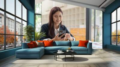 Smiling business asian woman using phone in office. Small business entrepreneur looking at her mobile phone and smiling. Wall mural