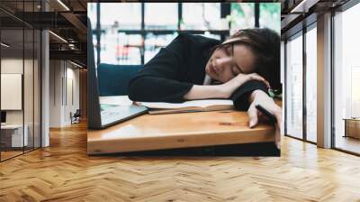 Tired or exhausted young business woman napping on working desk in front of her laptop in office Wall mural