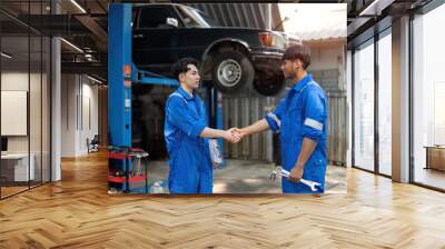 Two Asian automotive mechanic repairman handshake in garage. Vehicle service manager working in mechanics workshop, feel happy and success after check and maintenance car engine for customer. Wall mural