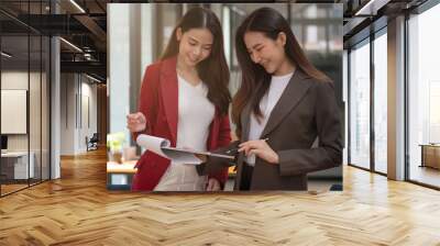 Two asian female collegues standing next to each other in an office, business meeting discussion concept Wall mural