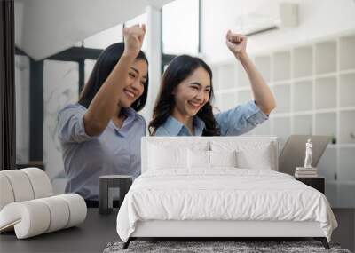 Two young businesswomen show joyful expression of success at work smiling happily with a laptop computer in a modern office Wall mural