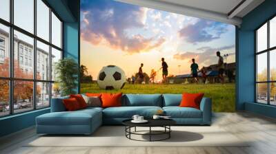 Action sport outdoors of kids having fun playing soccer football for exercise in community rural area under the twilight sunset sky. Fresh silhouette and vibrant image with anonymous people. Wall mural