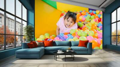 Smiling baby playing in the balls pool. Cute and happy girl. Picture for developmental in children concept. Wall mural