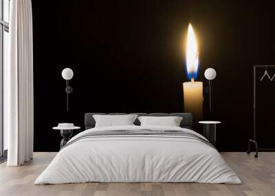 A single candle light glowing on a white candle on black background Wall mural