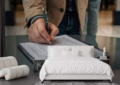 A close-up of a male hand of Caucasian descent writing in a notebook at a table. Wall mural