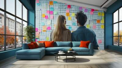 Two people brainstorming, viewing a wall covered in colorful sticky notes, illustrating collaborative idea generation and creative planning.. Wall mural