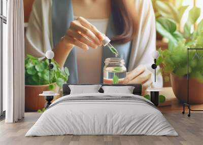  woman adding green extract from a dropper into a glass of water with green leaves, surrounded by plants.. Wall mural